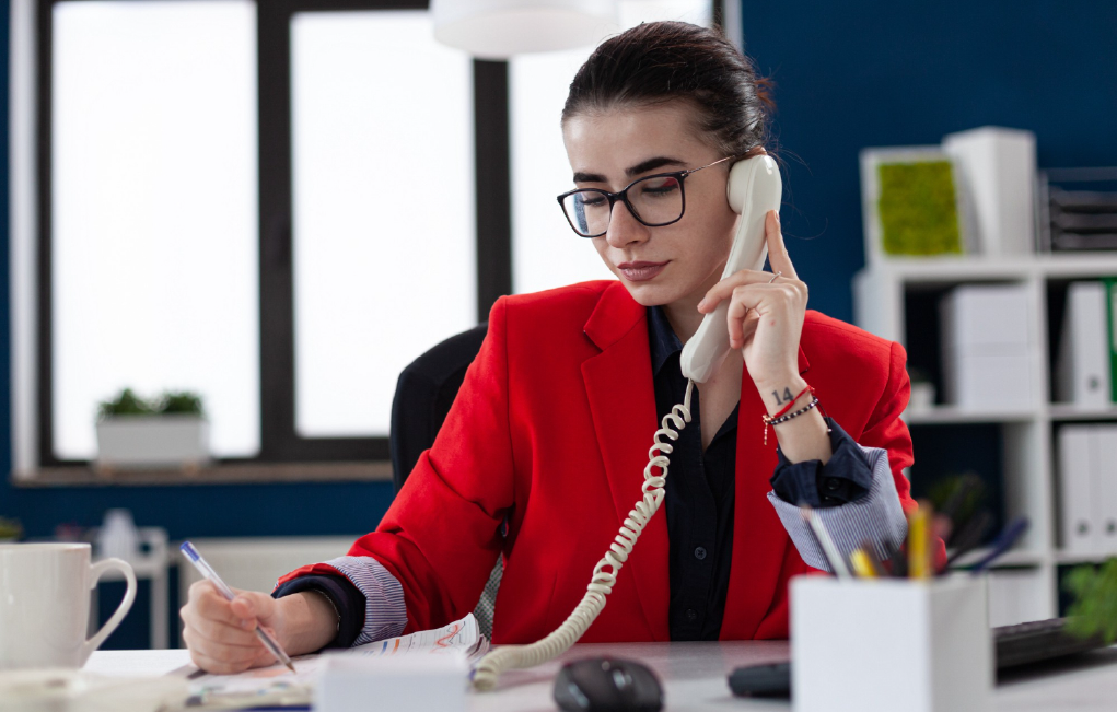 businesswoman taking notes on clipboard sitting at desk in corporate office while taking